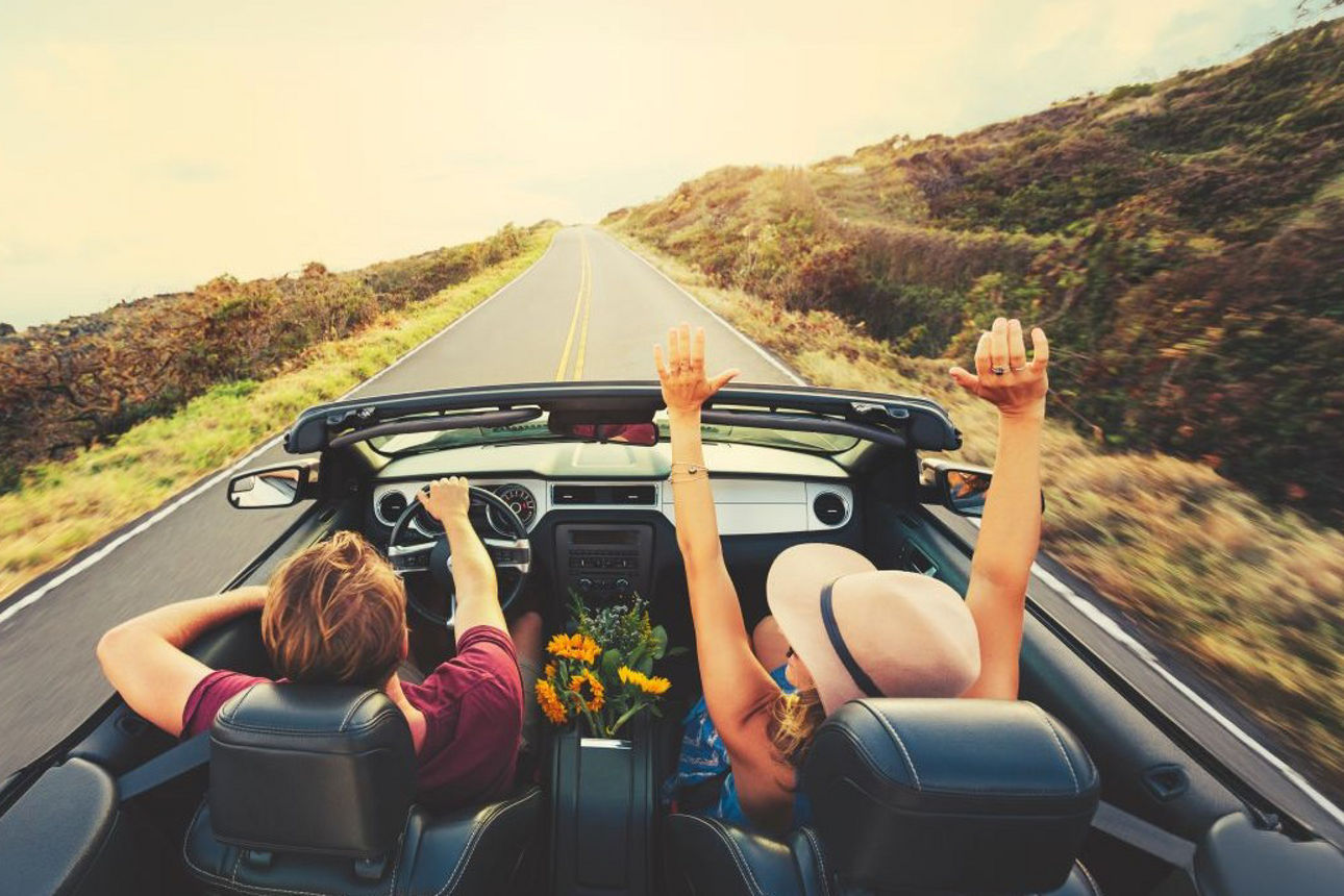 Pärchen fährt in einem Cabrio Richtung Sonnenuntergang