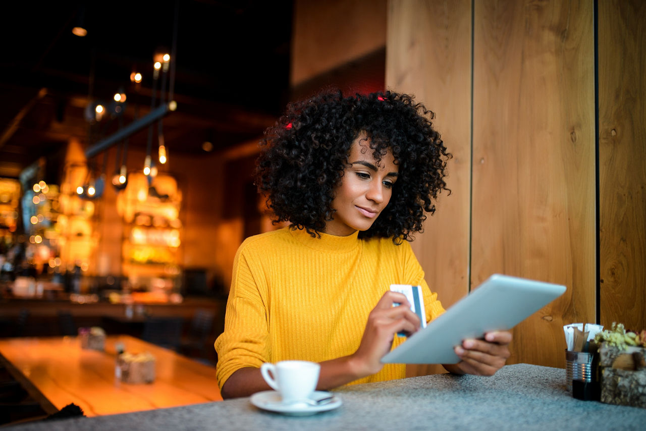 Eine junge Frau sitzt mit Tablet und Bankkarte in einem Cafe.
