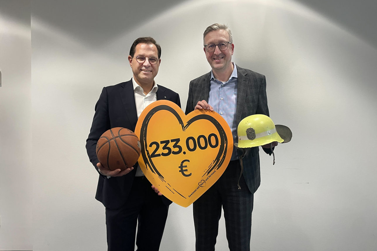 Der Vorstandsvorsitzende und der stellvertretende Vorsitzende der VR-Bank Main-Rhön stehen vor einer weißen Wand. Sie halten ein großes Schild in Herzform mit der Spendensumme von 233.000 Euro in den Händen.