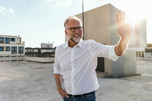 Mann auf Dachterrasse winkt jemandem lächelnd zu