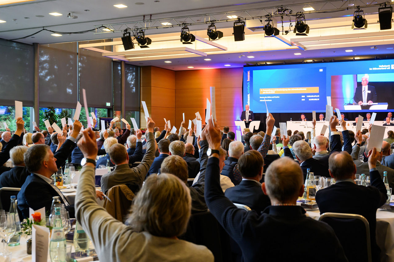 Mitglieder der Vertrerversammlung in einem großen Saal und heben ihre Hände mit einem Zettel in der Hand