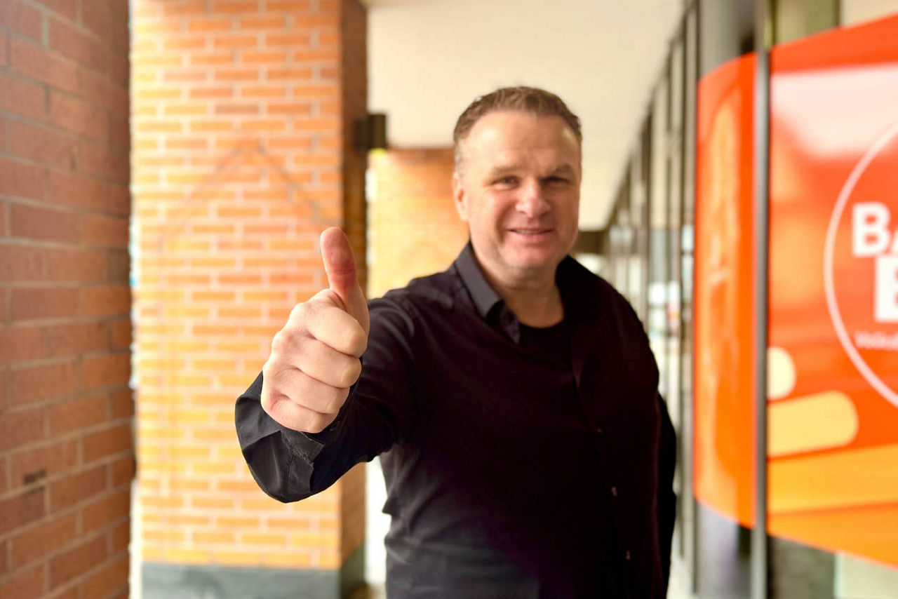 Sie sehen einen Mann in einem Schwarzen Hemd, der den Daumen hochstreckt.