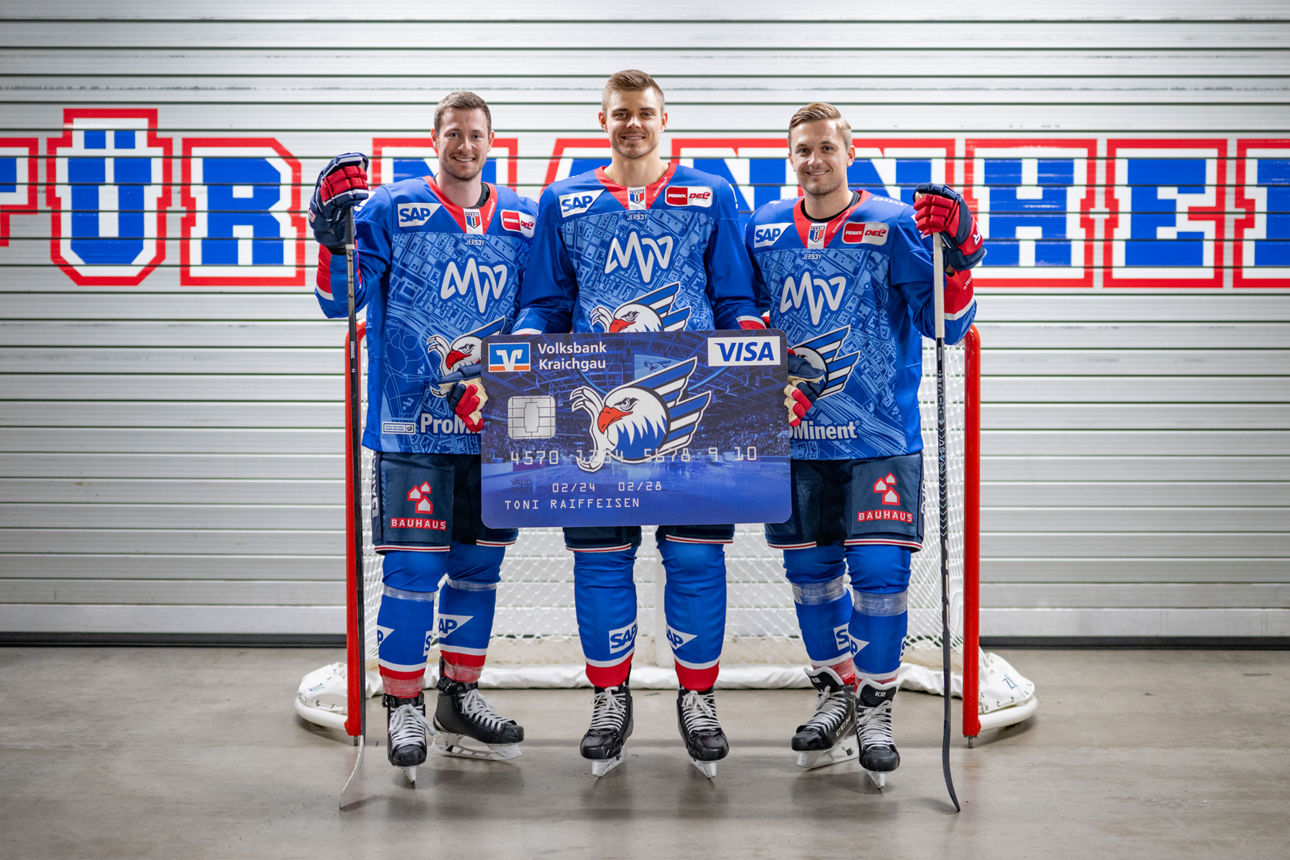 Drei Spieler der Adler Mannheim halten eine große Kreditkarte im Adler-Design.