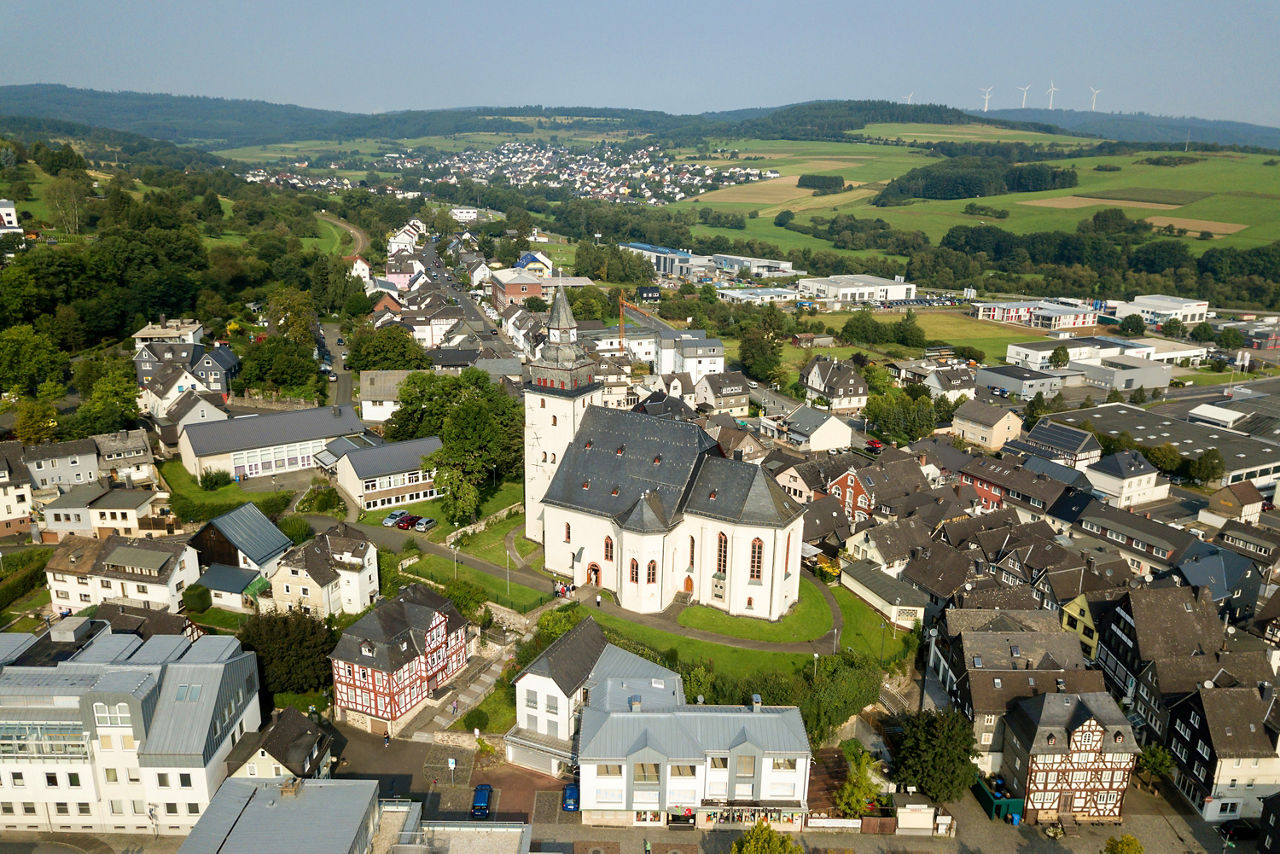 Luftaufnahme der Stadt Haiger mit der großen Kirche im Zentrum, umgeben von Wohnhäusern, Fachwerkbauten und Industriegebieten in grüner Hügellandschaft.