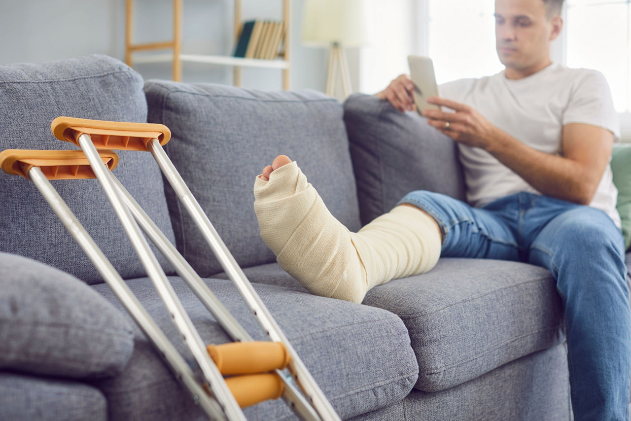 Mann mit gebrochenem Bein sitzt auf Sofa