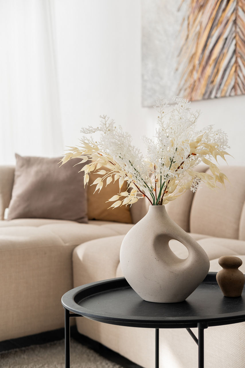 A stylish black table holds a unique vase filled with dried flowers in a cozy space.