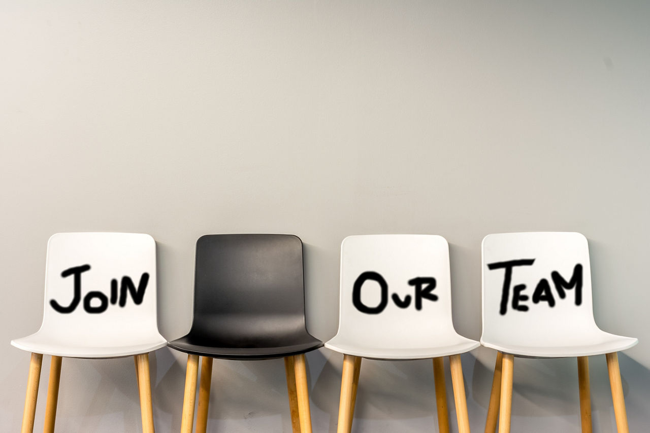 Drei weiße und ein grauer Stuhl. Auf den weißen Stühlen steht jeweils ein Wort geschrieben, die den Satz ergeben: Join our Team