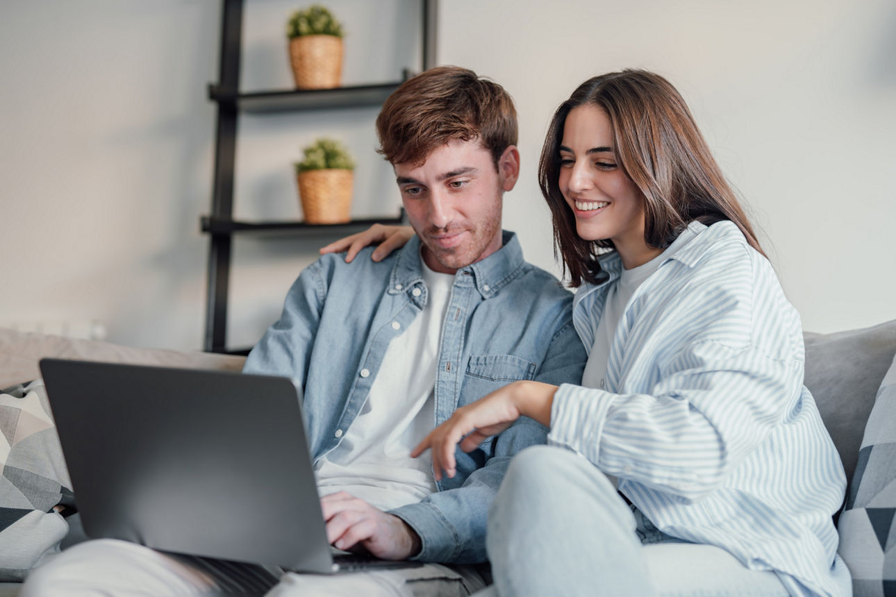 Junges Paar sitzt auf dem Sofa und blickt auf einen Laptop