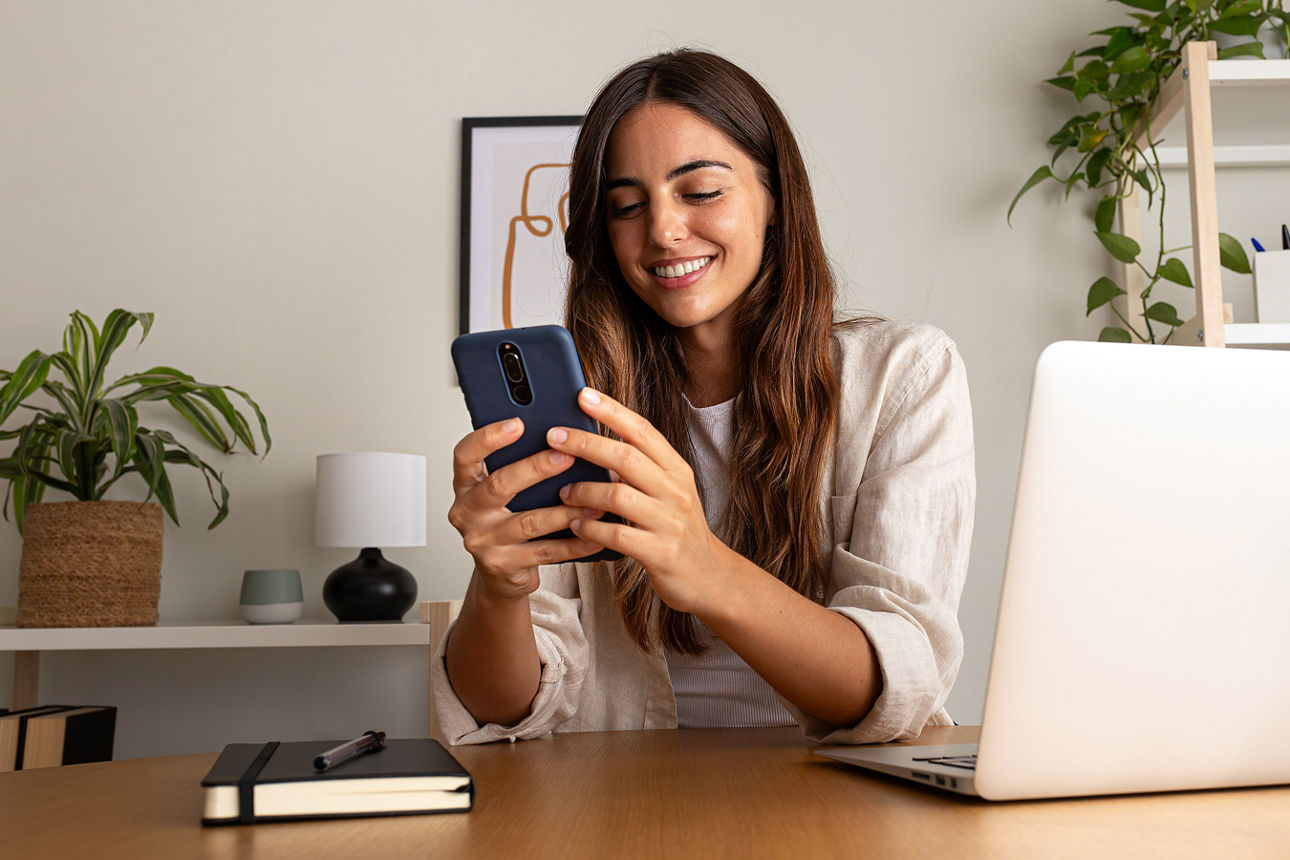Frau mit Handy in der Hand sitzt am Laptop