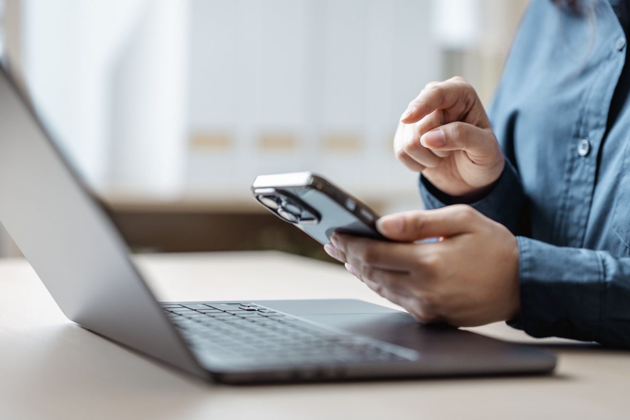 Mann sitzt vor seinem Laptop und tippt auf seinem Handy