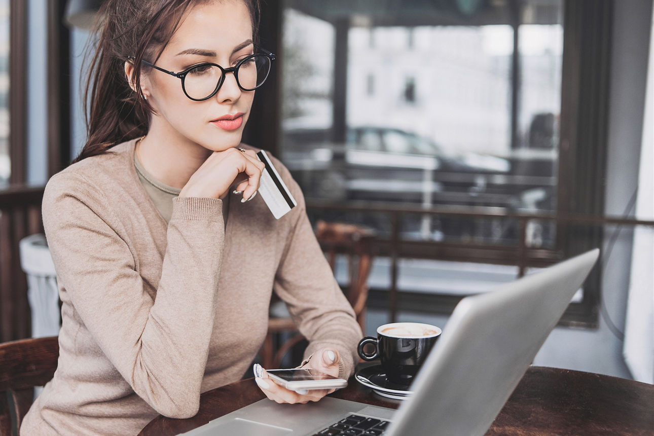 Frau mit Smartphone und Karte vor Laptop