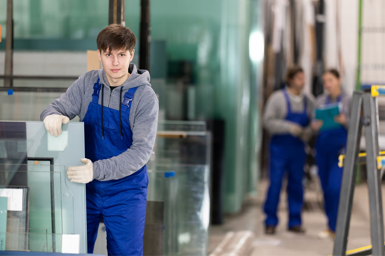 Ein junger Mann in blauer Latzhose ist an der Arbeit und sortiert gerade Glasplatten.
