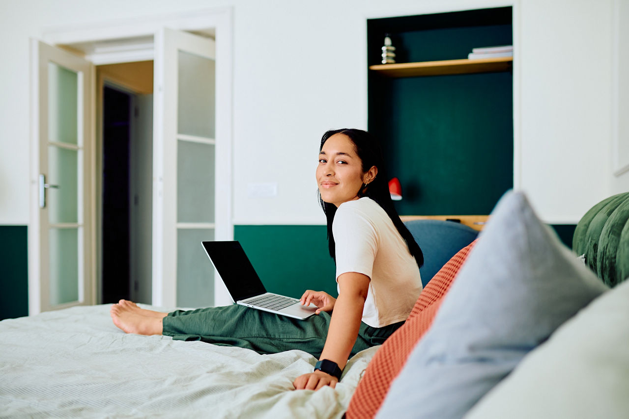 Junge Frau sitzt mit Laptop auf dem Bett