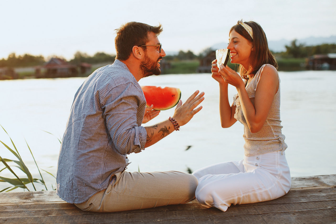 Junges Paar isst Wassermelone am Fluss während des Sonnenuntergangs