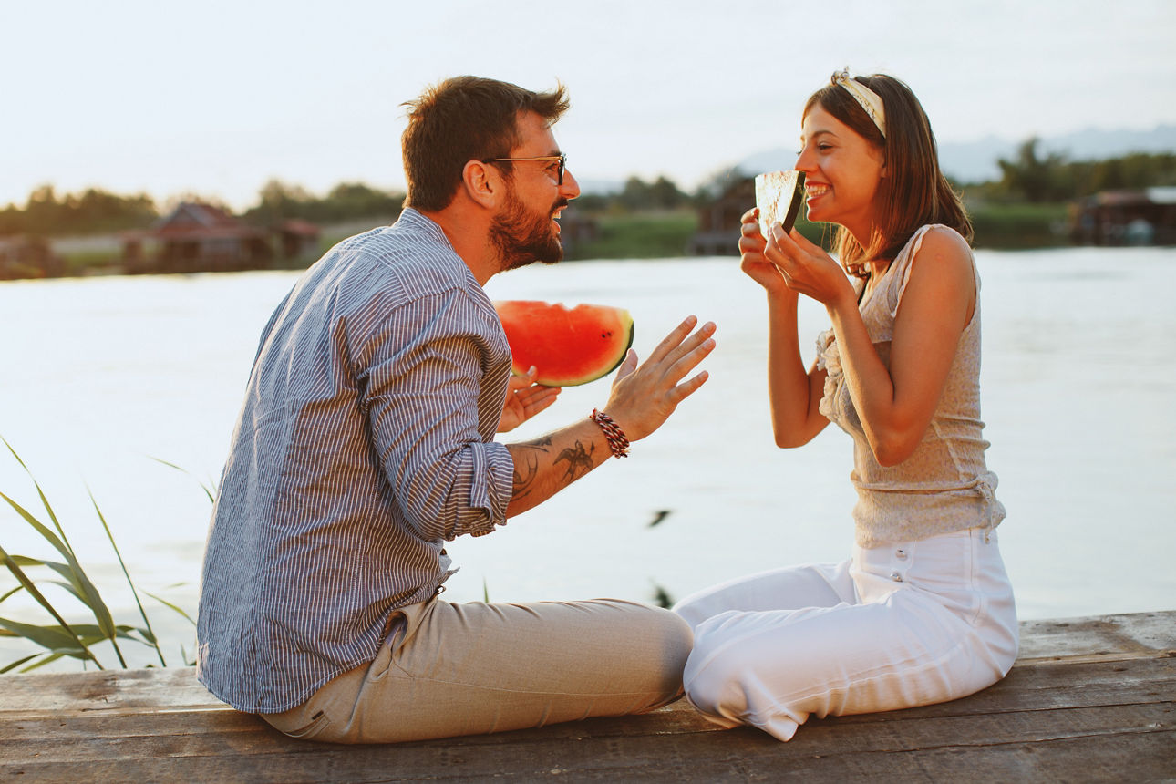 Junges Paar isst Wassermelone am Fluss während des Sonnenuntergangs