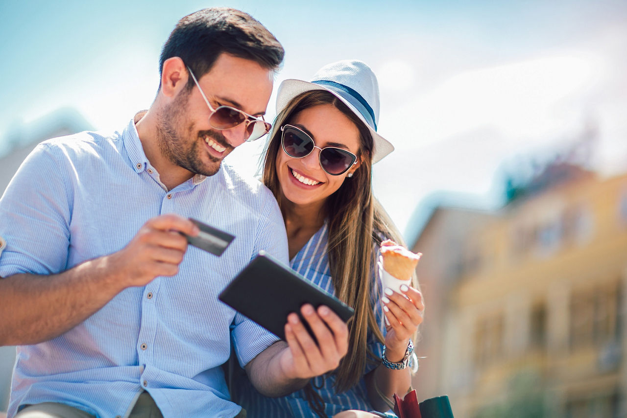 Paar sitzt mit Tablet, Kreditkarte und Eis in der Sonne