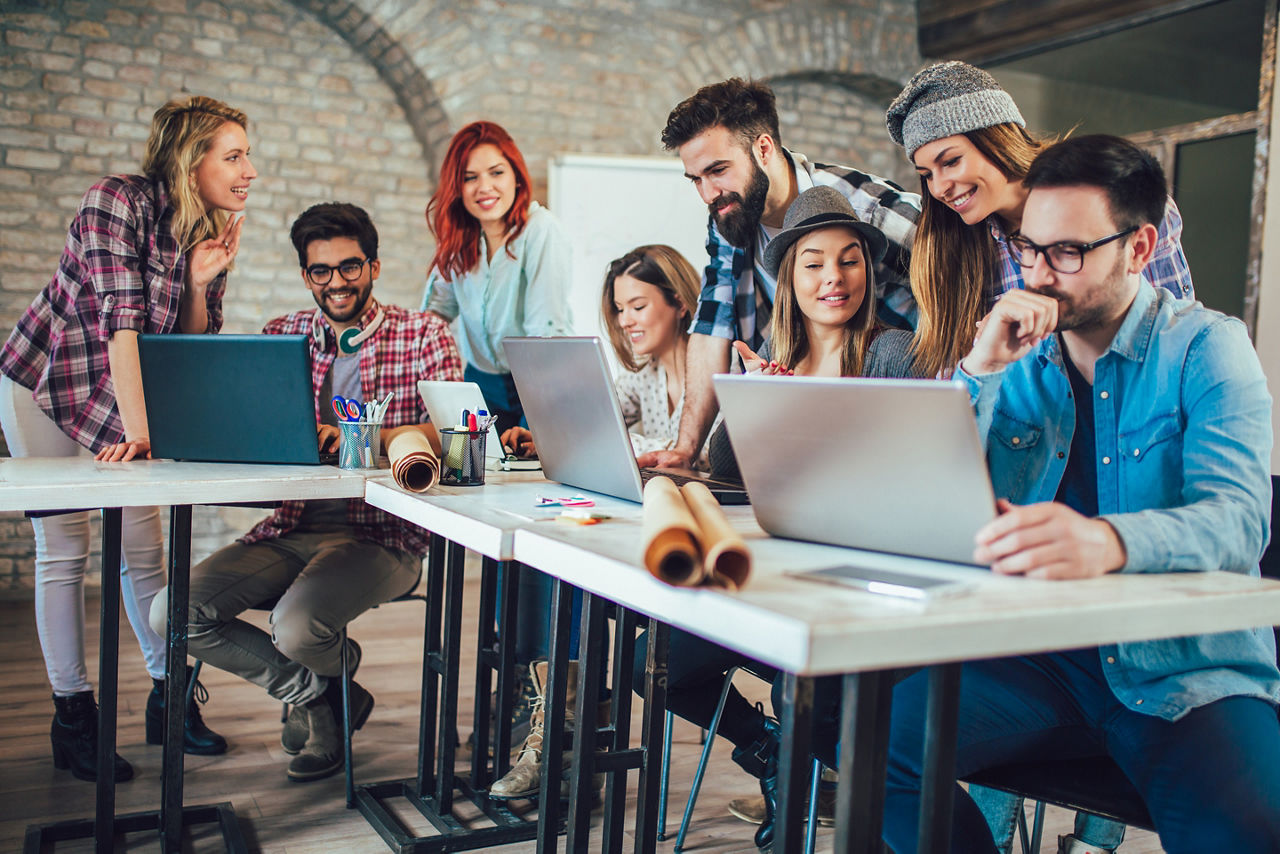 Junge Menschen schauen sitzend oder stehend auf Laptops