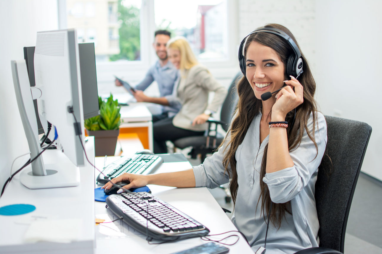 Frau mit Headset sitz lächelnd an einem Computer