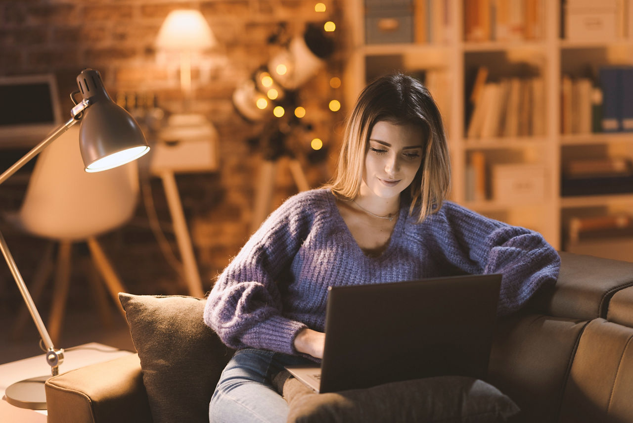 Young attractive woman watching on her laptop, living room interior in the background