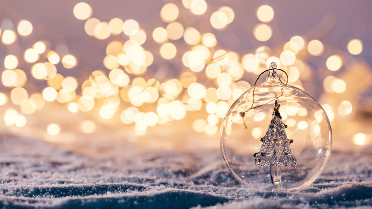 Glasweihnachtskugel mit Tannenbaum vor Lichtermeer auf Schneeuntergrund.