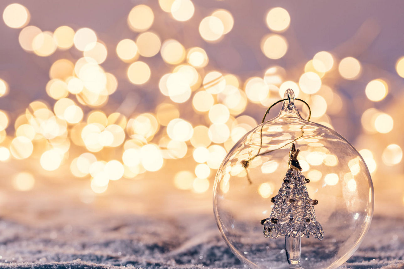 Glasweihnachtskugel mit Tannenbaum vor Lichtermeer auf Schneeuntergrund.