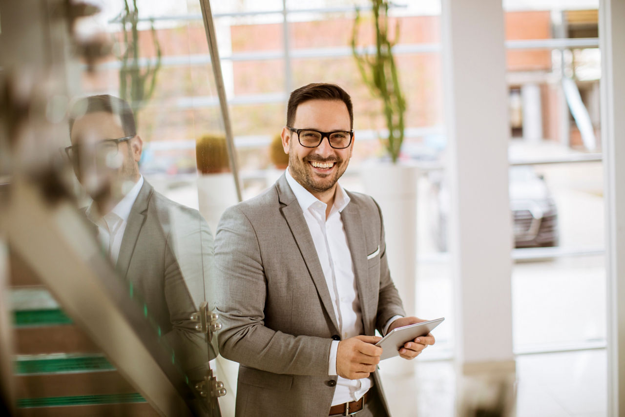 Happy businessman dressed in suit standing  in modern office  and using tablet