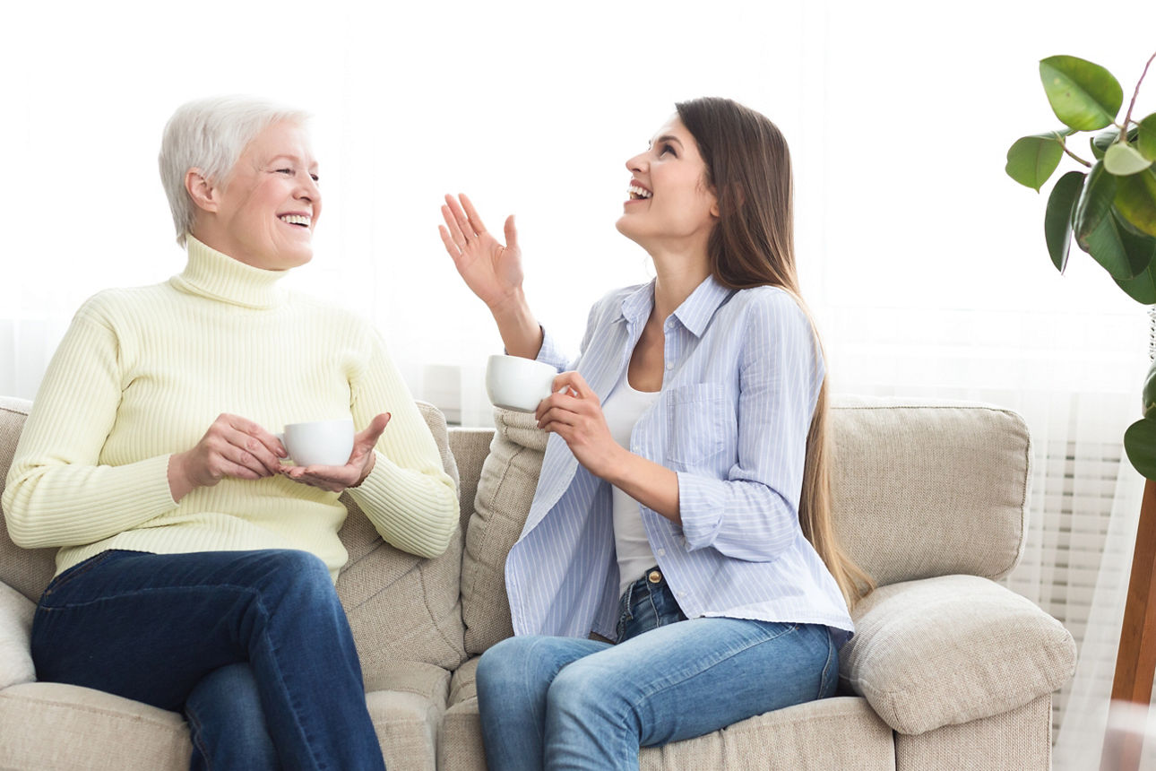 Mother and daughter drinking coffee and talking on couch at home