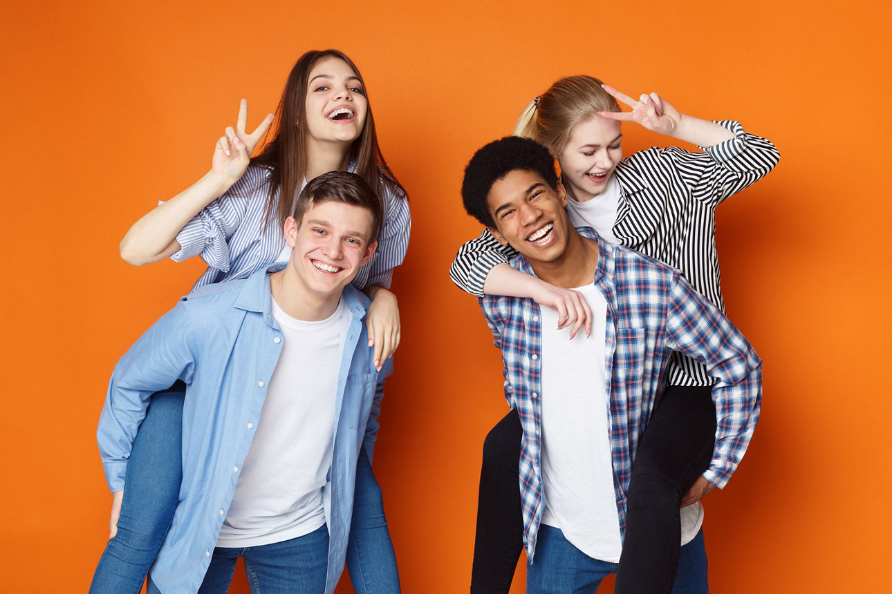 Freunde die Spaß haben. Jungen haben die Mädchen Huckepack vor einem orangenen Hintergrund. 