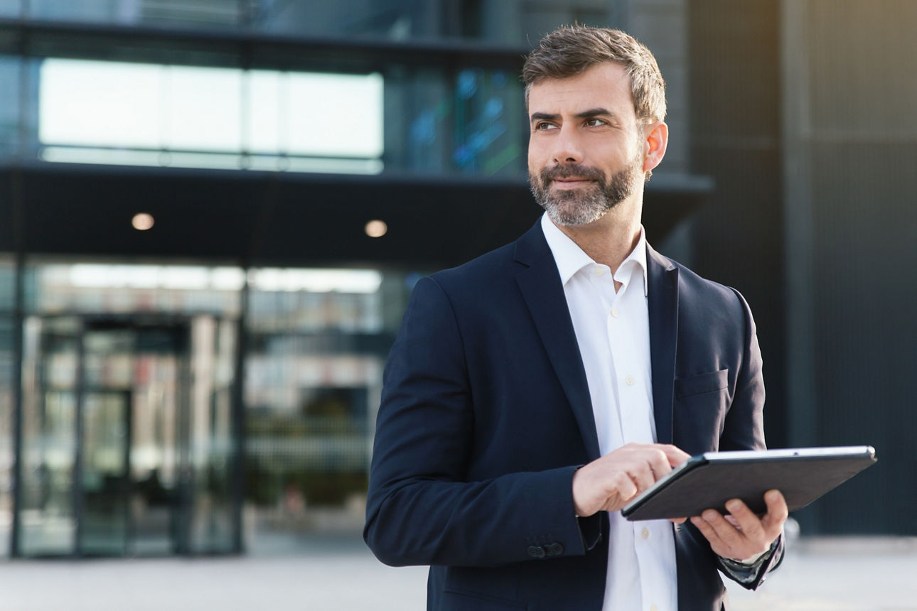 Ein Mann steht vor einem Gebäude und hält ein Tablet in der Hand