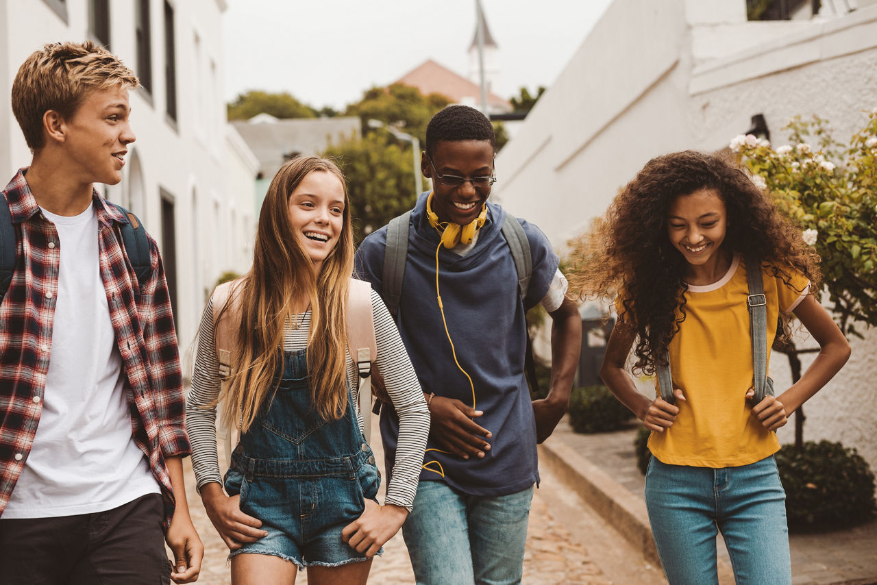 Group of multiethnic college friends walking in the street. Smiling teenage friends wearing college bags walking outdoors and talking.