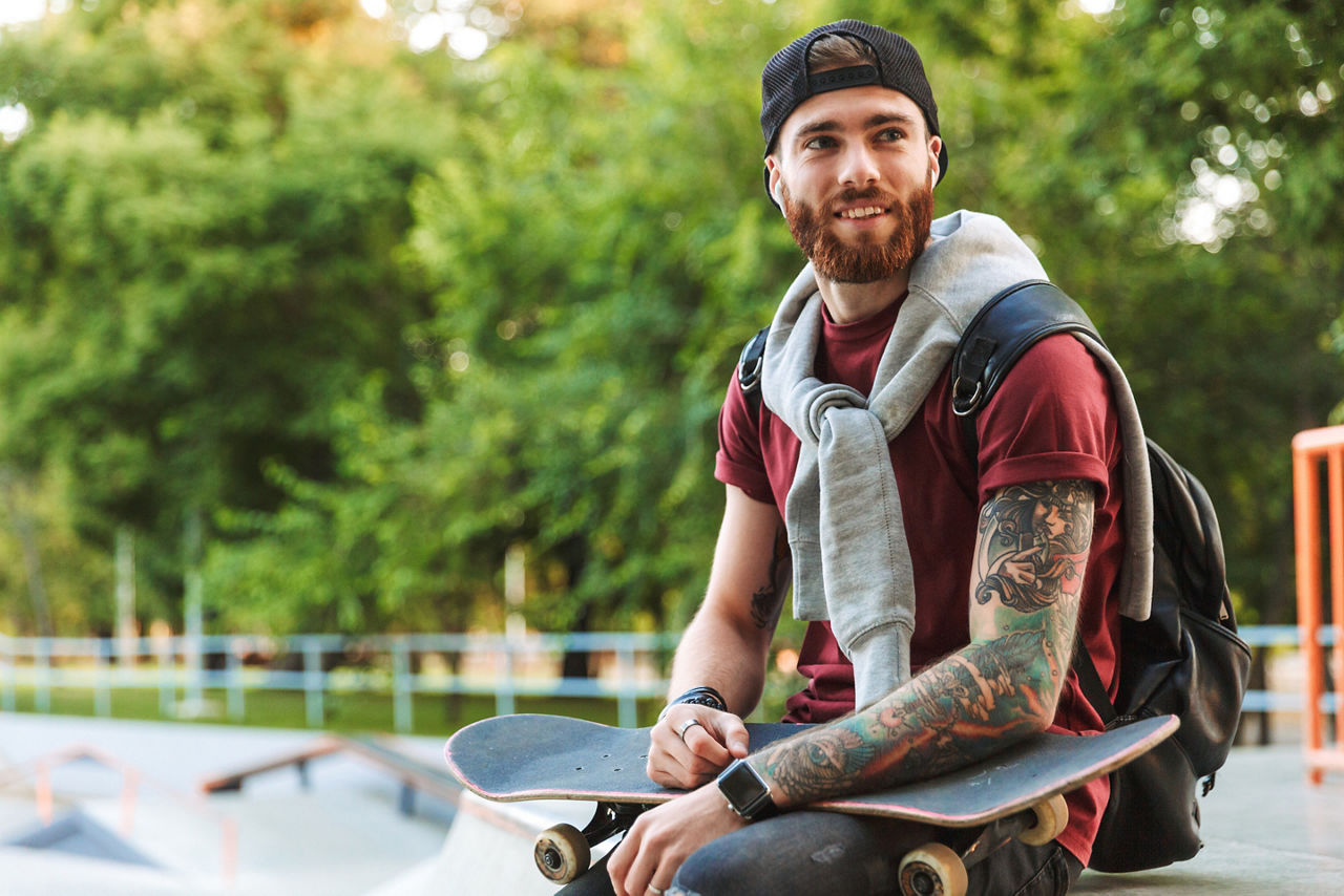 Junger Mann sitzt mit seinem Skateboard auf einer Skaterrampe