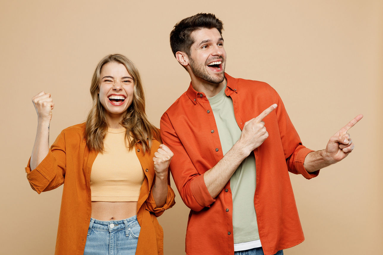 Young couple two friends family man woman wear casual clothes point index finger aside on area mock up do winner gesture together isolated on pastel plain light beige color background studio portrait