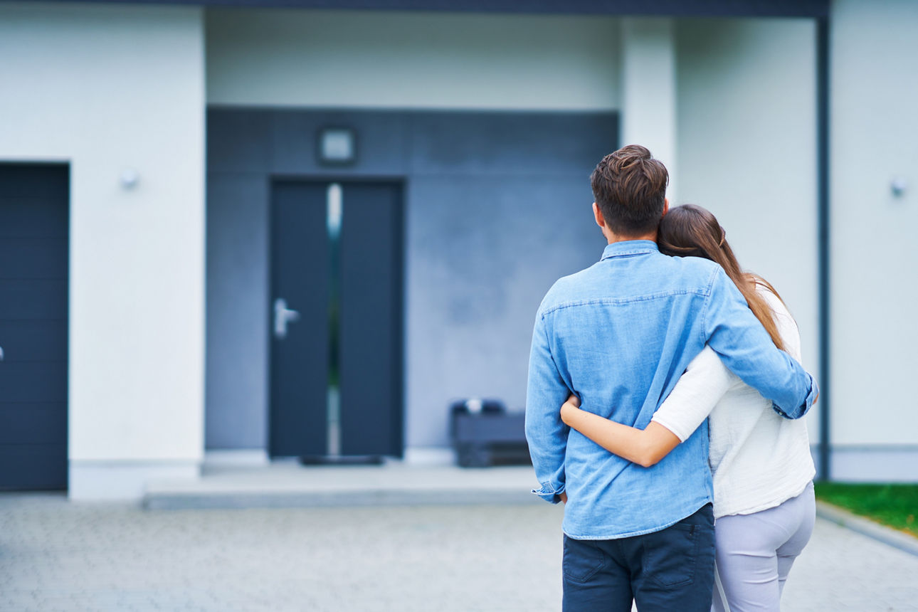 Mann und Frau stehen Arm in Arm vorm Eingang eines Hauses