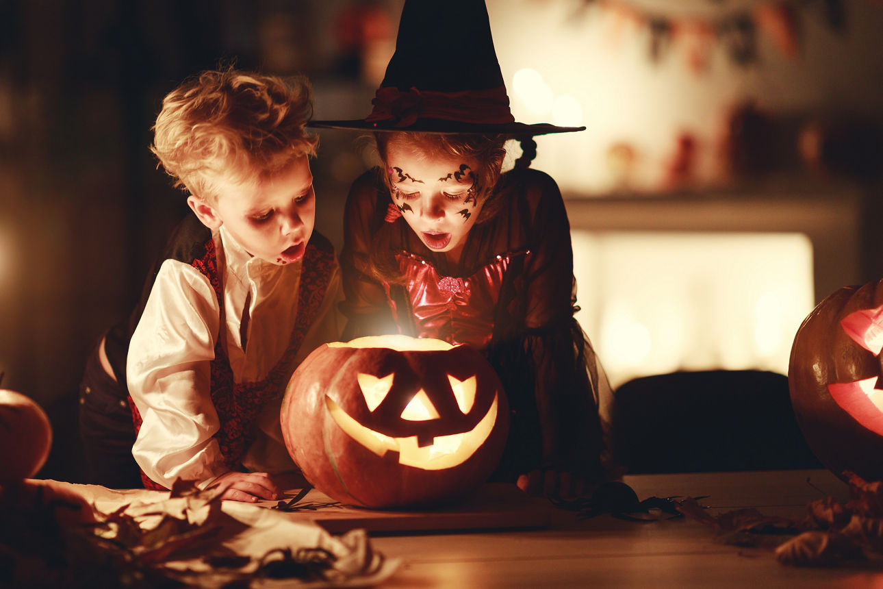 Ein Junge und ein Mädchen schauen erstaunt in einen leuchtenden Kürbis