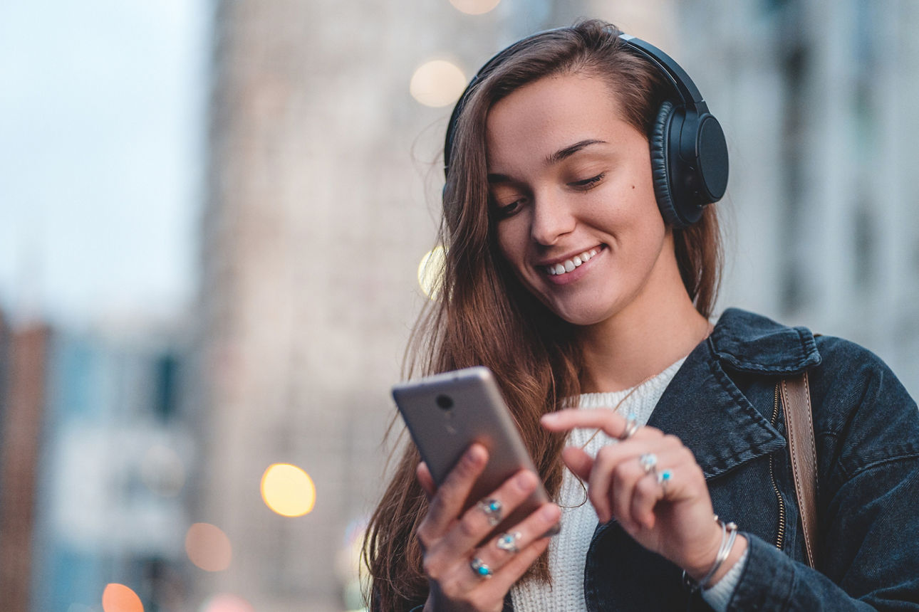 Frau mit Kopfhörer schaut lächelnd auf ihr Smartphone