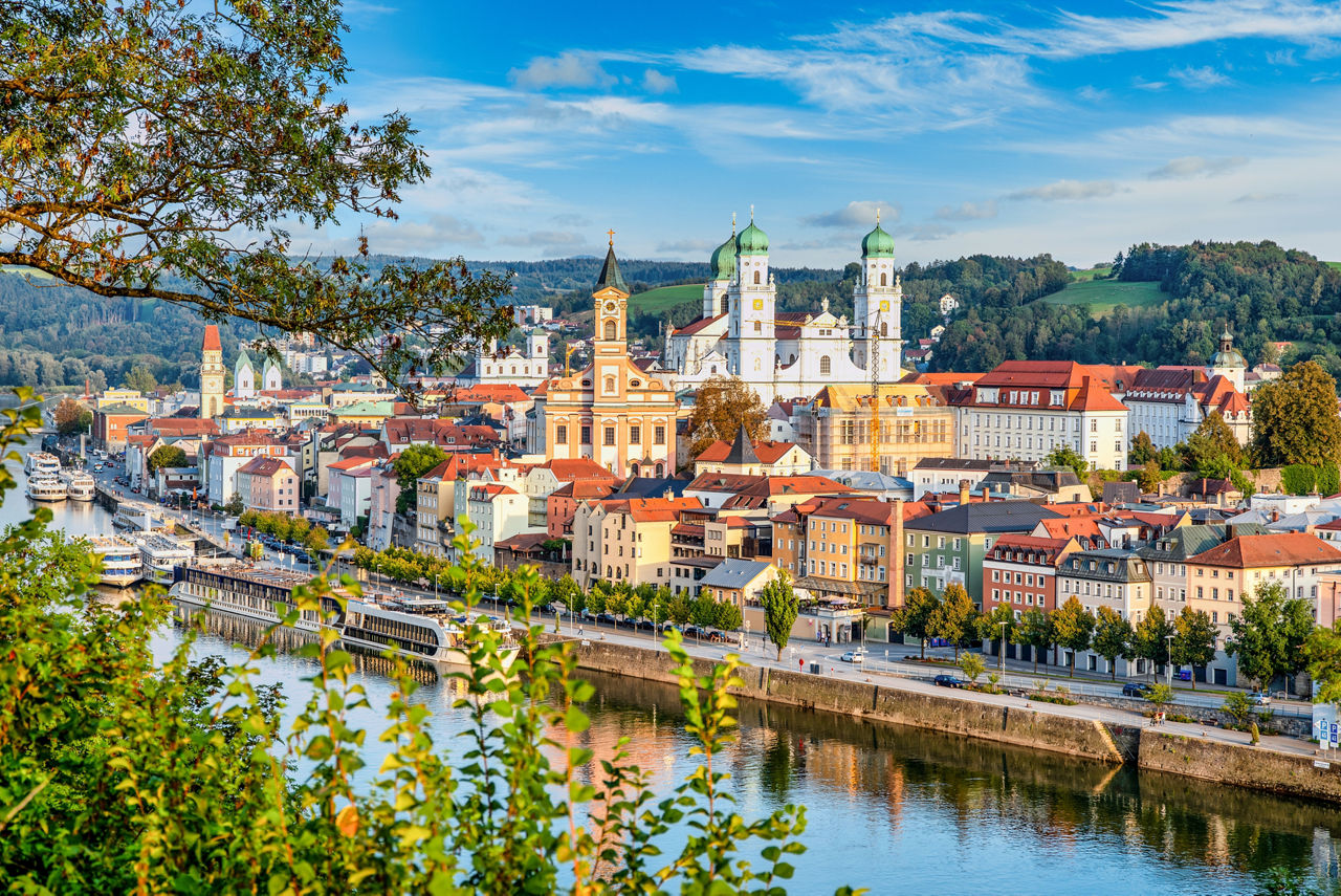 Blick auf die Altstadt Passau an der Uferpromenade auf den dominaten weißen Dom, mehrer kleine Schiffe befinden sich im Fluss