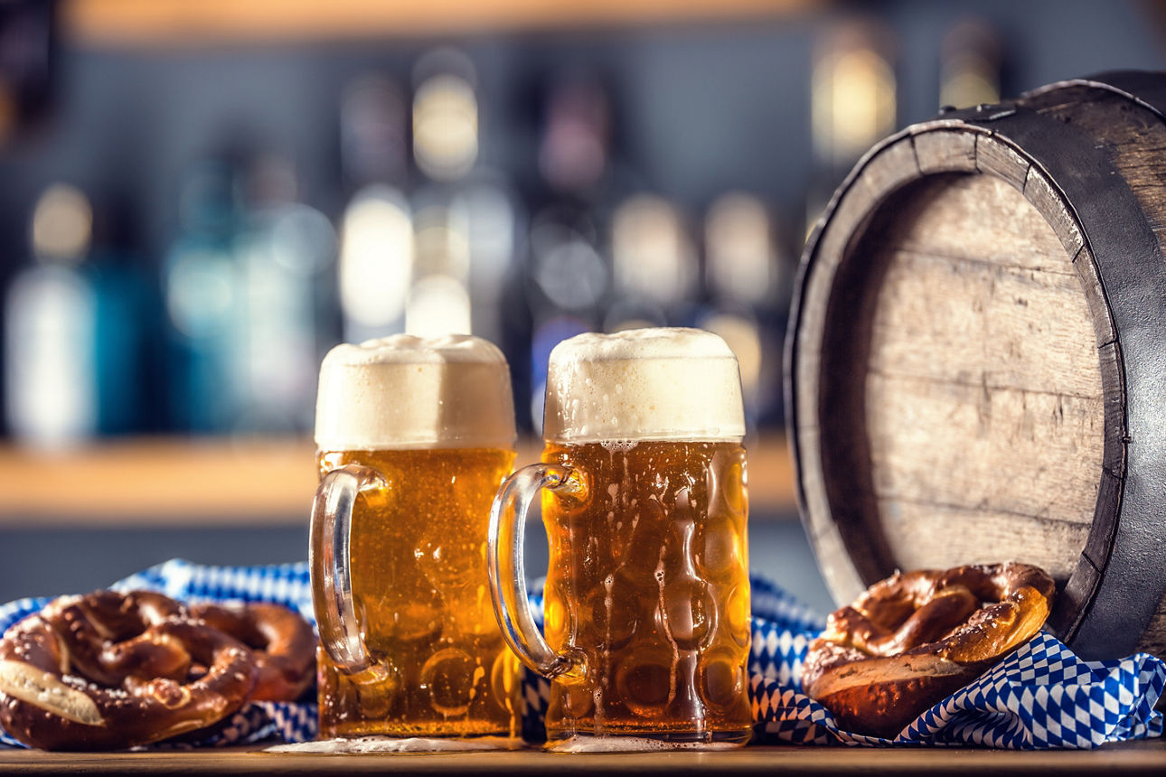 Oktoberfest two large beer with pretzel wooden barrel and blue tablecloth.