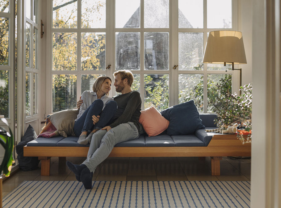Ehepaar sitzt im sonnendurchfluteten Wohnzimmer auf einem Sofa