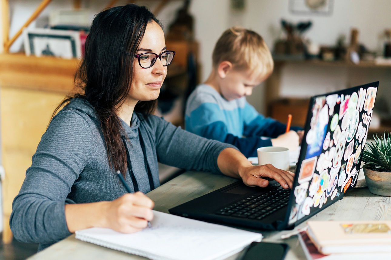 Eine Frau arbeitet am Laptop. Das Kind neben ihr malt