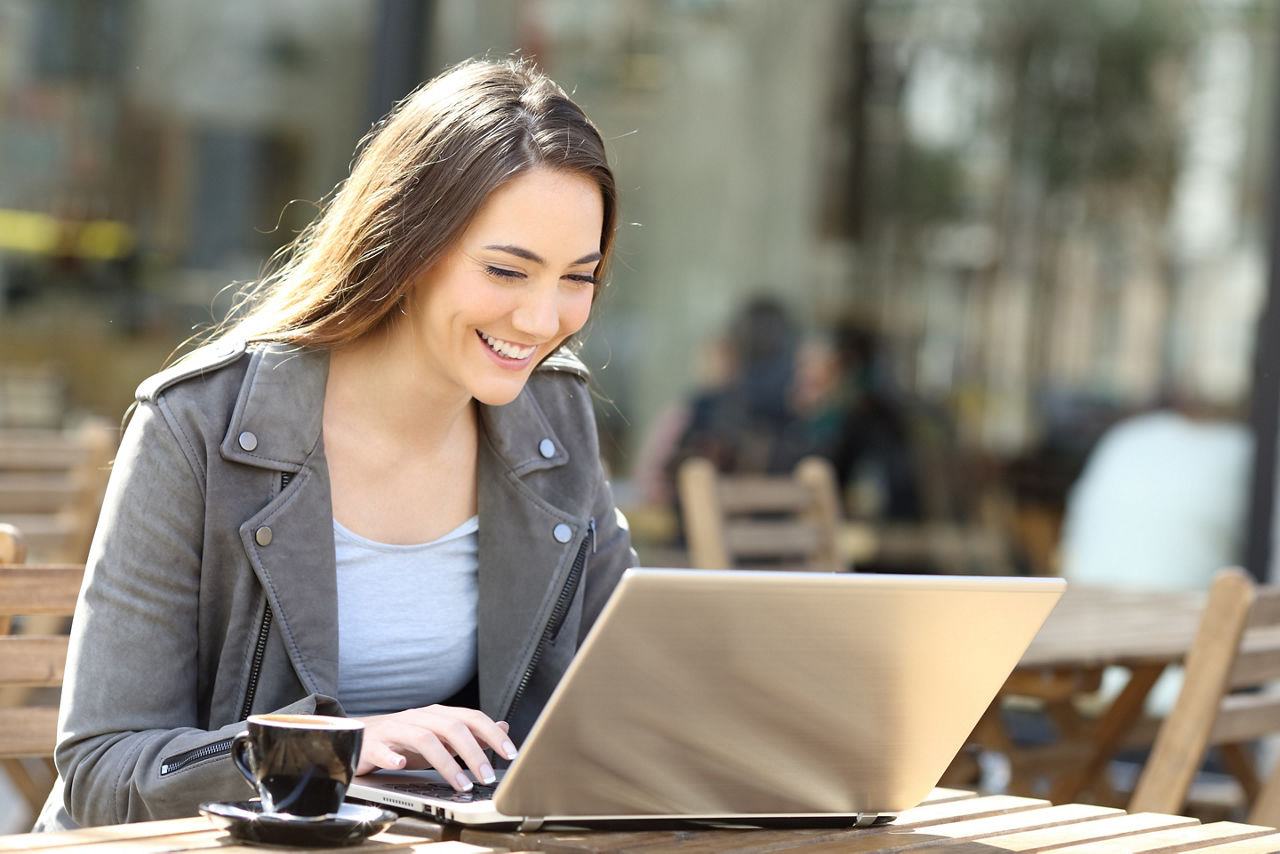 Lächelnde Frau sitzt im Cafe und tippt auf dem Laptop