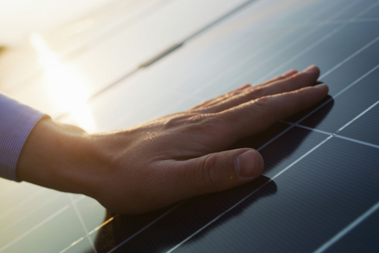 Eine Hand berührt ein Solarpanel im Sonnenlicht und symbolisiert nachhaltige Energie.