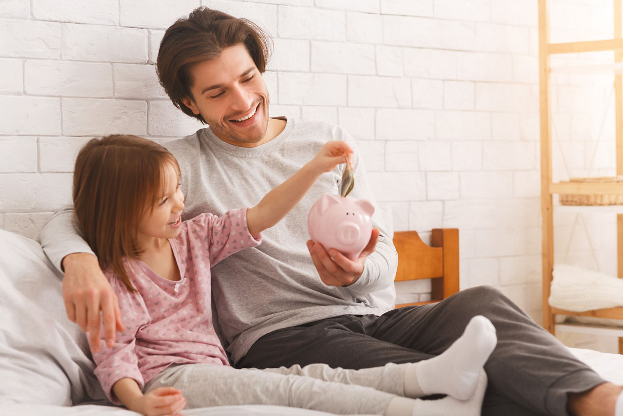 Vater und Tochter sitzen mit Sparschwein auf der Couch