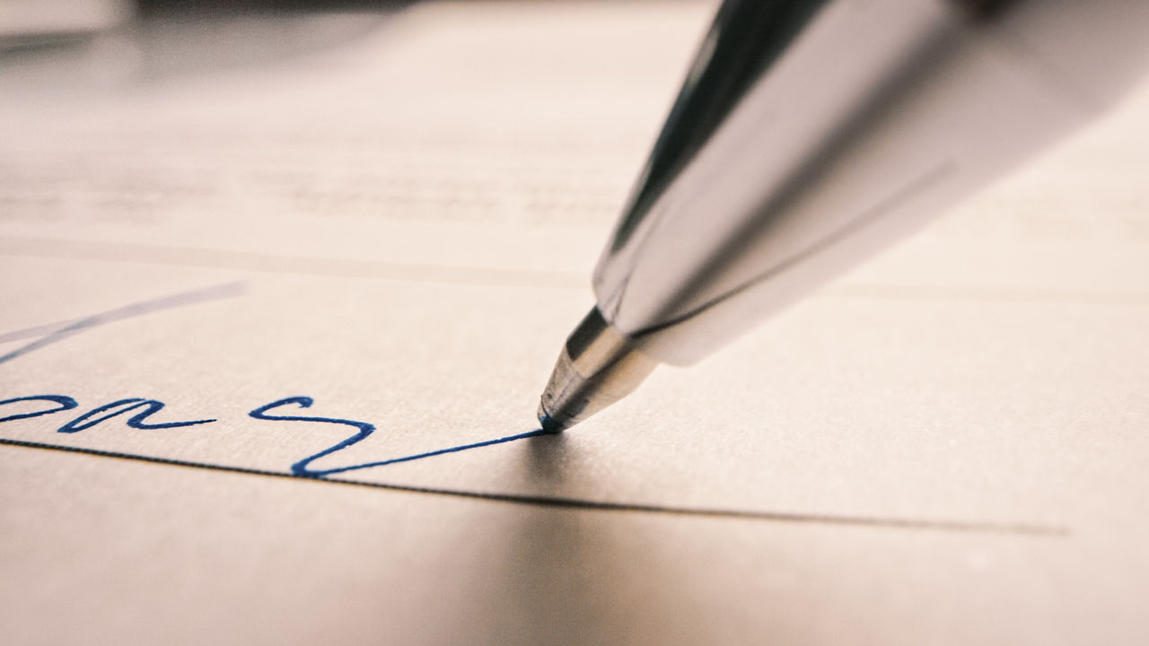 Die Spitze des Stifts ist zu sehen und eine handschriftliche Signatur 