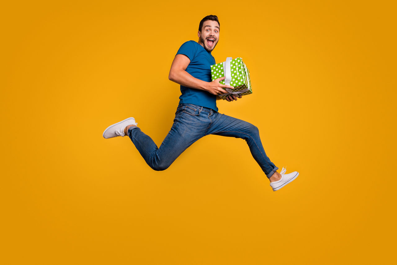 Full length body size view of his he nice attractive crazy overjoyed, cheerful cheery guy jumping holding in hands giftbox isolated over bright vivid shine vibrant yellow color background