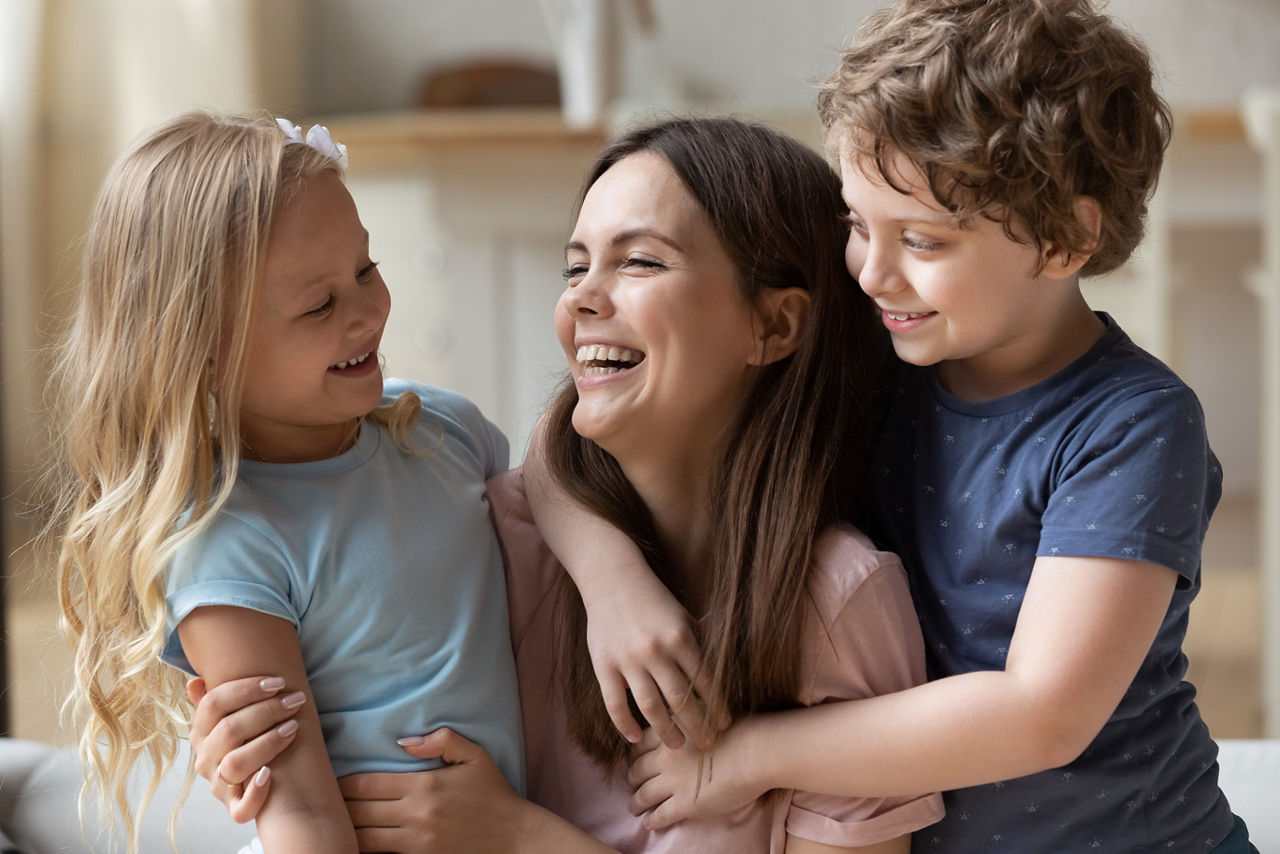 Eine junge Frau strahlt, während sie von zwei Kindern umarmt wird.