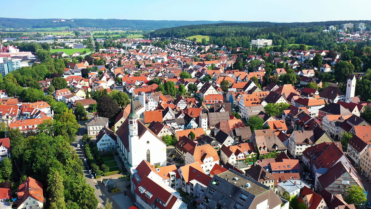 Luftaufnahme von Leutkirchmit Kirche, Wohnhäusern, Straßen sowie weitläufigen Feldern und Wäldern in der Umgebung.