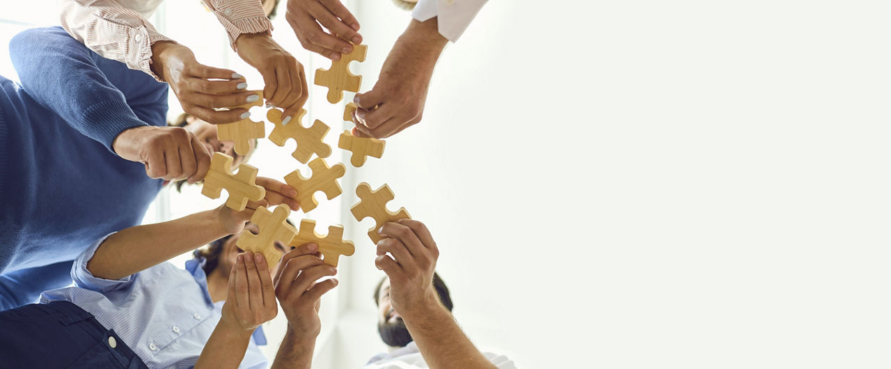Personengruppe im Kreis, die verschiedene Puzzleteile hält