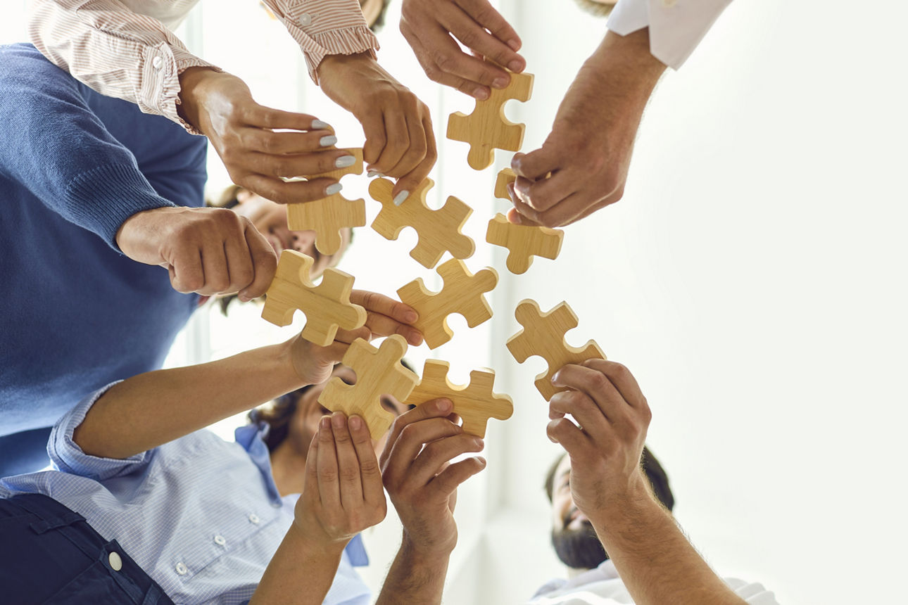 Personengruppe im Kreis, die verschiedene Puzzleteile hält