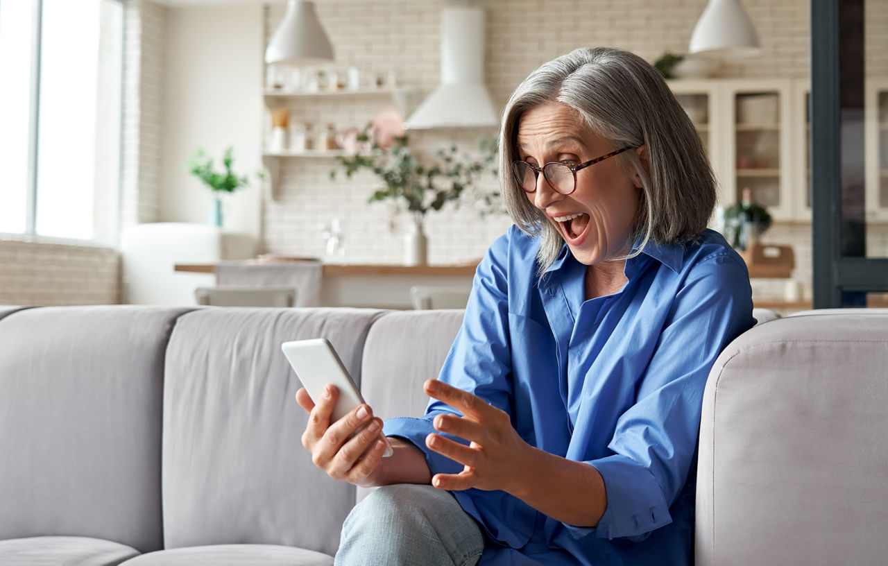 Frau die positiv überrascht vom Leistungsumfang Ihres Kontomodell ist, welches sie auf Ihrem Smartphone sieht.