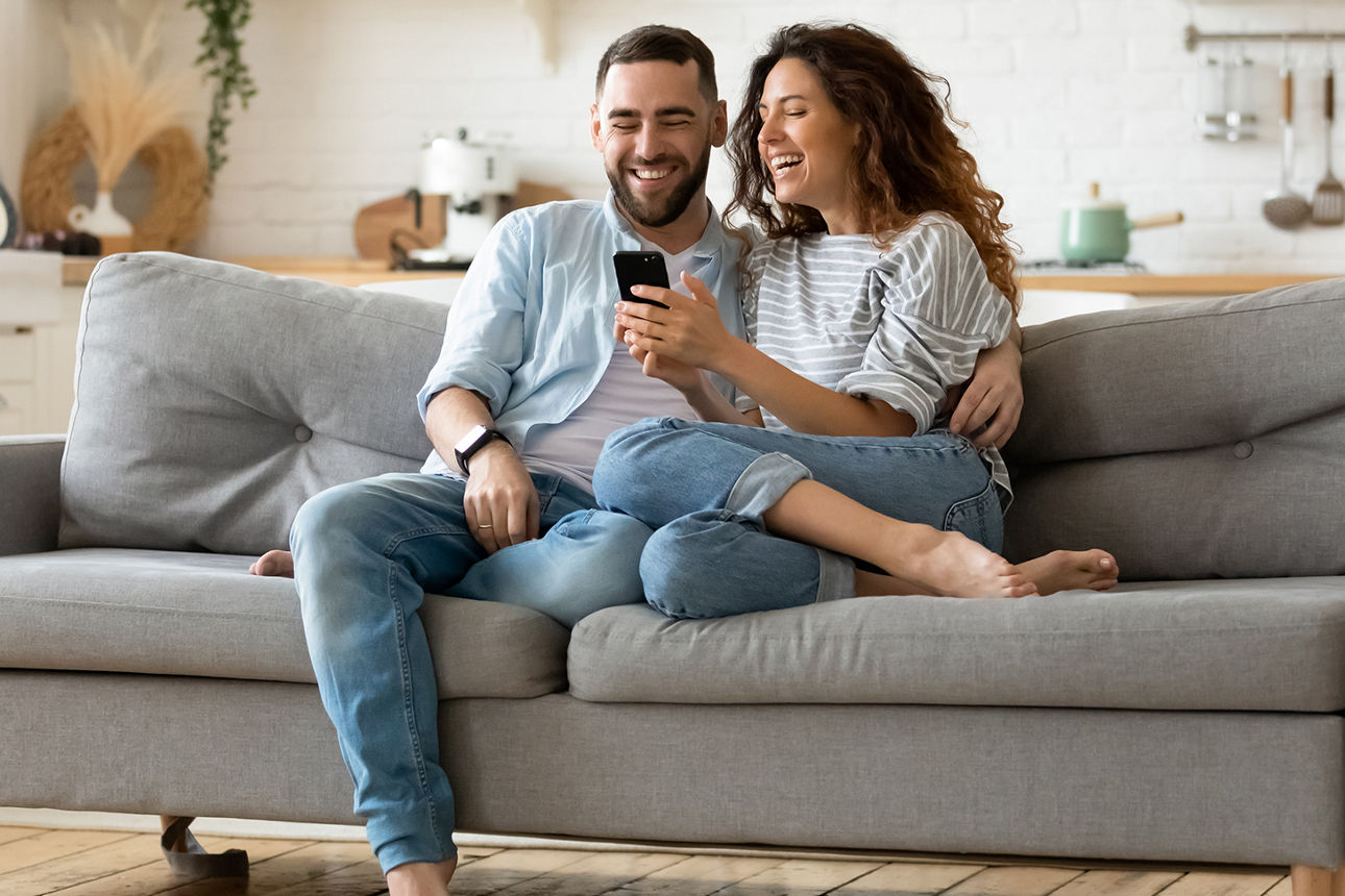Frau und Mann sitzen zusammen auf einer Couch und schauen erfreut auf ein Smartphone